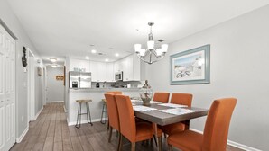 A modern kitchen with white cabinets, a central island, and a dining area with orange chairs.