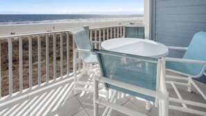 A balcony with a view of the beach, white railings, and two blue chairs.