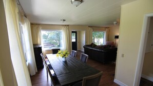 A dining area with a wooden table, chairs, and a vase of flowers. There is a kitchen area with a counter and chairs in the background. - Garden Creek Retreat - Remodeled Home with Luxury Furnishings (Challis)