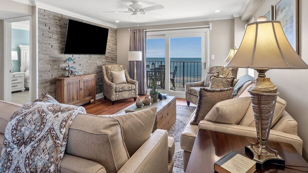 A spacious living room with a large flat-screen TV, comfortable seating, a ceiling fan, and a view of the ocean through large sliding doors. - Upgraded oceanfront condo with pool, kid's pool and private balcony for plenty of sunrises & sunsets (North Myrtle Beach)