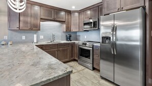 A modern kitchen with wooden cabinets, a stainless steel refrigerator, a microwave, an oven, and a granite countertop. - Upgraded oceanfront condo with pool, kid's pool and private balcony for plenty of sunrises & sunsets (North Myrtle Beach)