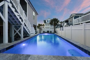 A swimming pool with a tiled edge, surrounded by a white fence, and adjacent to a multi-story building with a staircase.