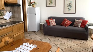 A compact living space with a kitchenette, a grey sofa with patterned cushions, and two framed artworks on the wall. - Il Mulino Pdl (Ponte di Legno)
