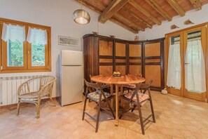 A cozy kitchen with a round wooden table, four chairs, a refrigerator, and a window with curtains. - CASA I FORNI ( EX SASSI TURCHINI) - BILO CASA I FORNI ( SASSI TURCHINI) (Porto Azzurro)