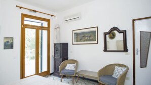 Una habitación con una cama, dos sillas de mimbre, un cuadro enmarco, un espejo y un equipo de aire acondicionado.