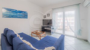 A living room with a blue sofa, a small table, a TV, and a large window with curtains.