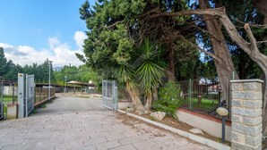 A paved pathway leading to a gated entrance with a stone wall and metal fence.