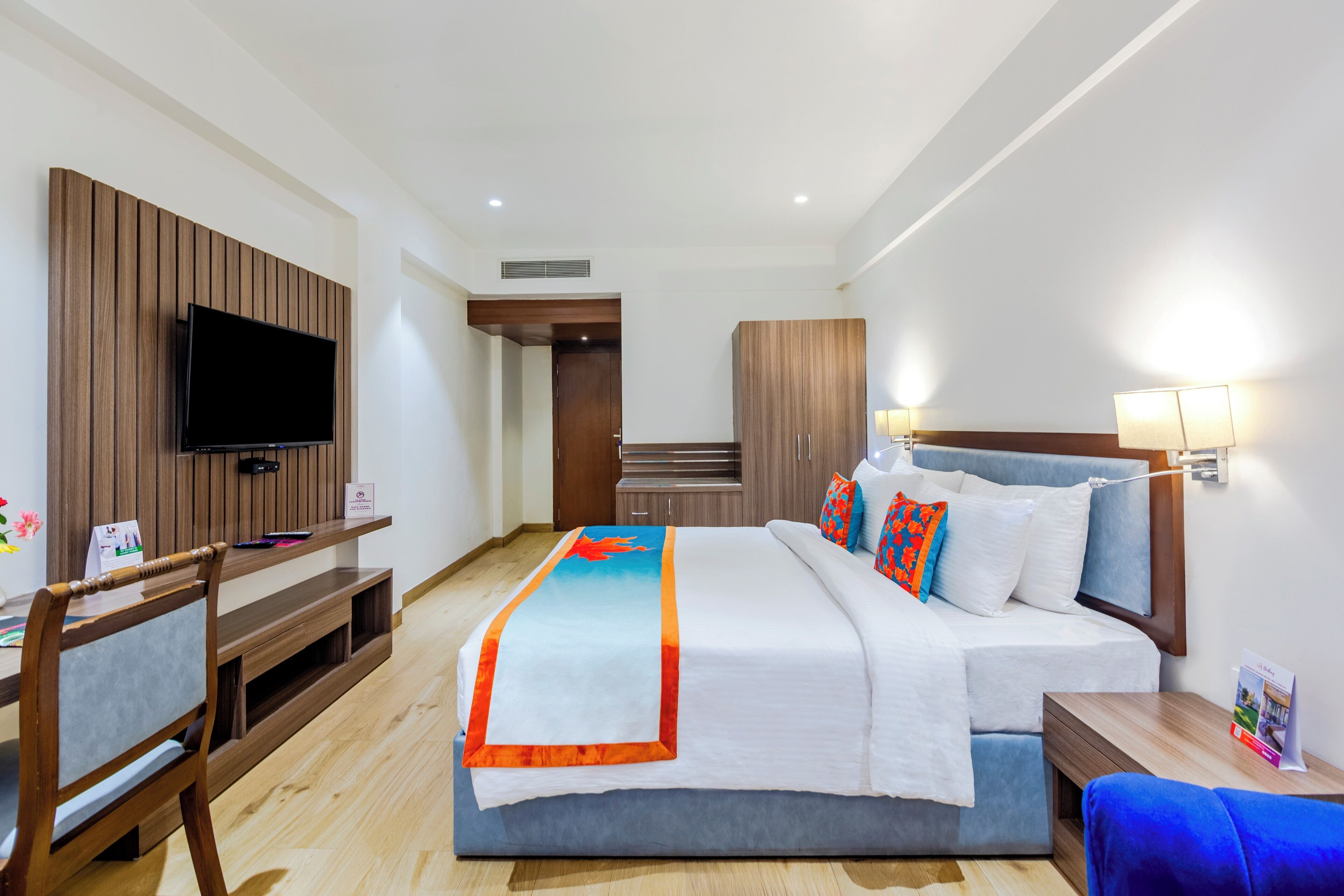 A modern hotel room with a large bed, a TV mounted on the wall, a desk with a chair, and a wardrobe.
