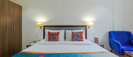 Camera d'albergo con un letto, due cuscini, un comodino, una lampada, una sedia blu e un armadio in legno.