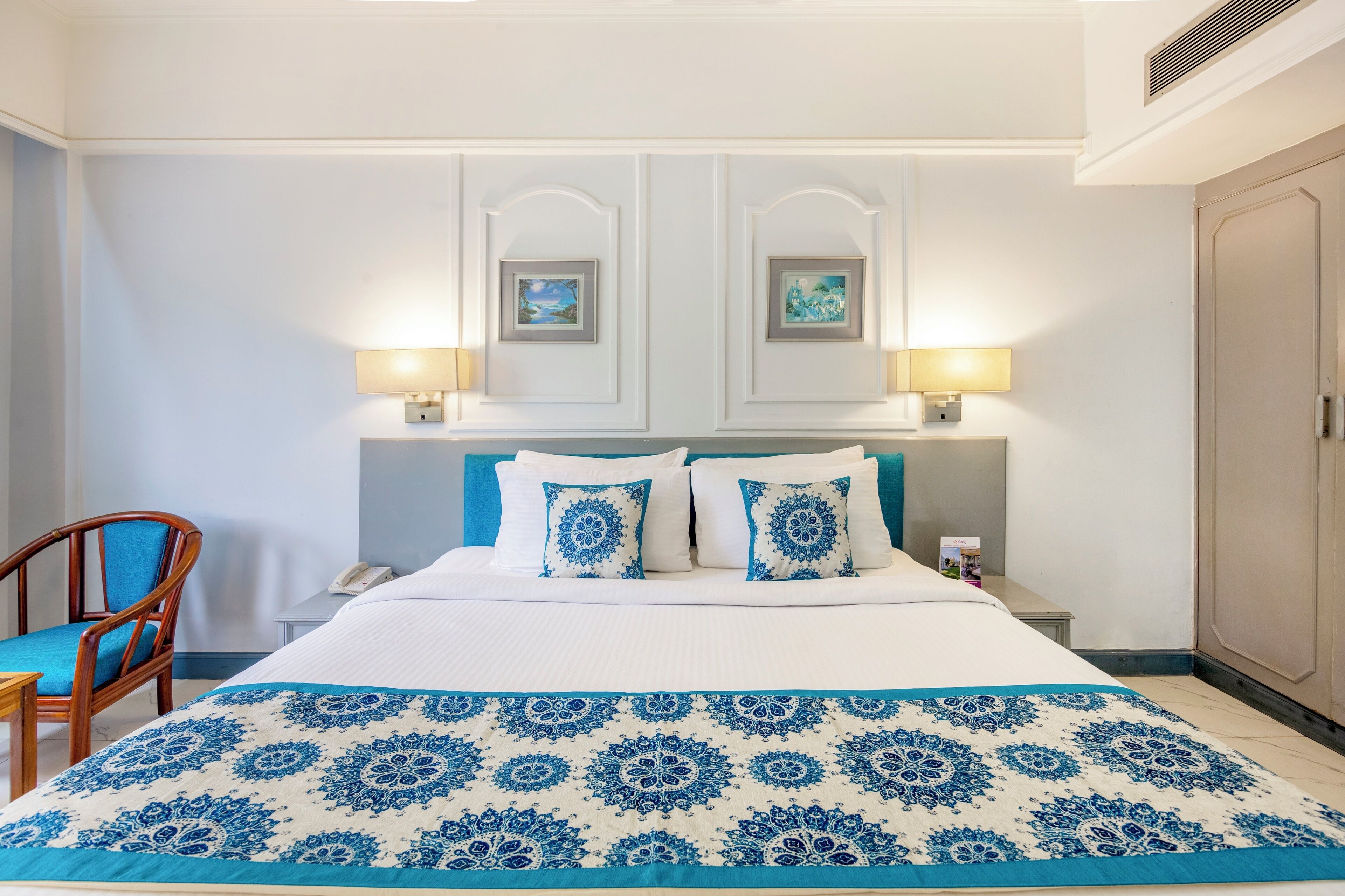 Una habitación de hotel con una cama grande, dos lámparas de noche, una silla y un armario.