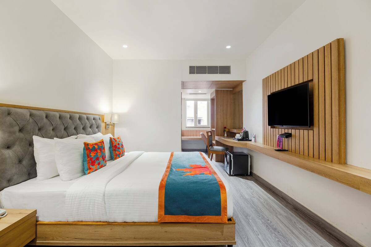 Une chambre d’hôtel avec un grand lit, un téléviseur fixé au mur, un bureau avec une chaise et une vue sur l’extérieur.