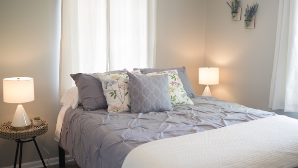 A neatly made bed with a grey duvet and white throw, flanked by two bedside lamps on a woven side table. - Orange Tree Cottage- Entire Cottage, Cute and Charming! (Pensacola)