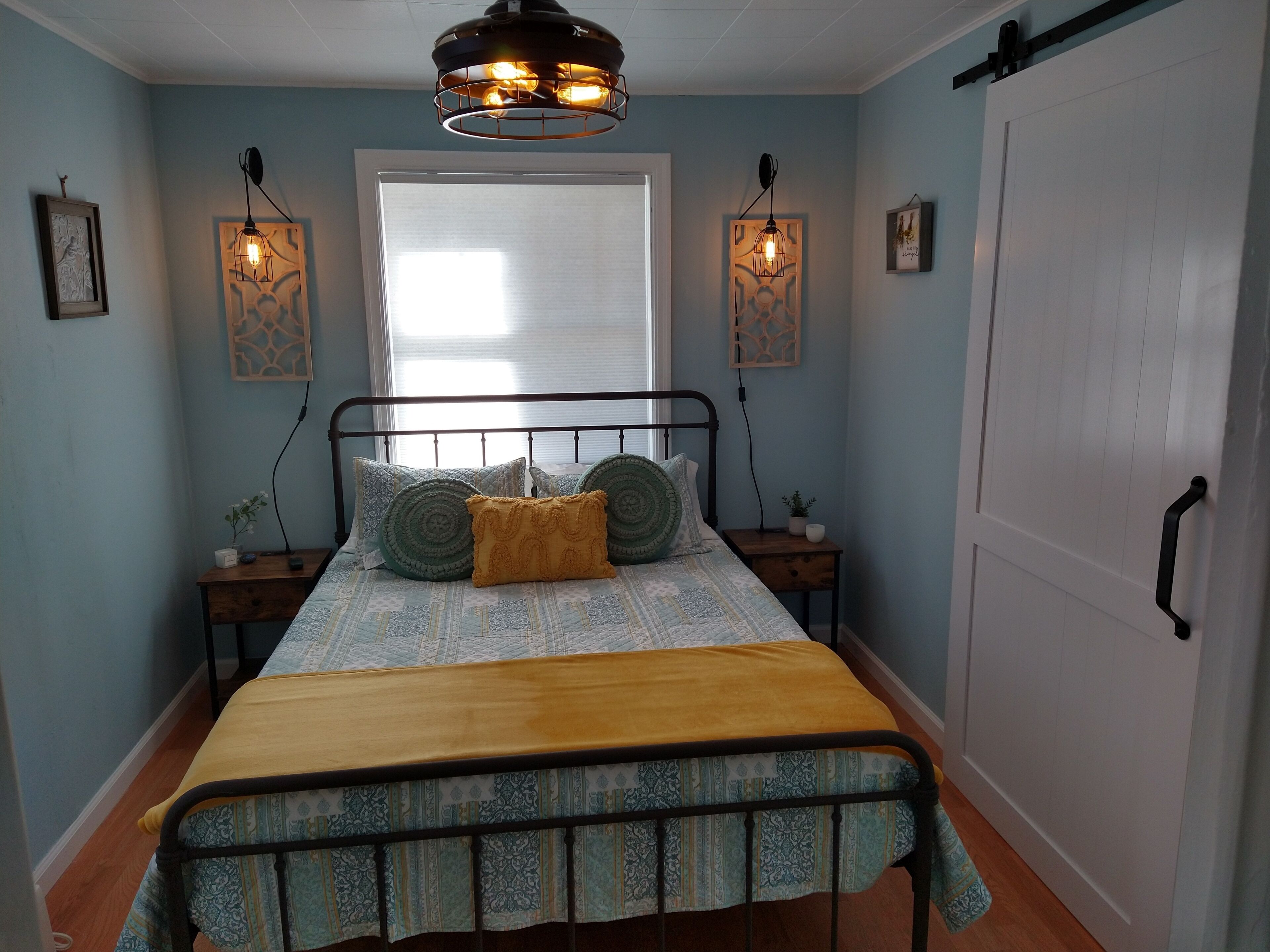 Une chambre à coucher comprenant un lit, des tables de chevet, une fenêtre et des luminaires fixés au mur.