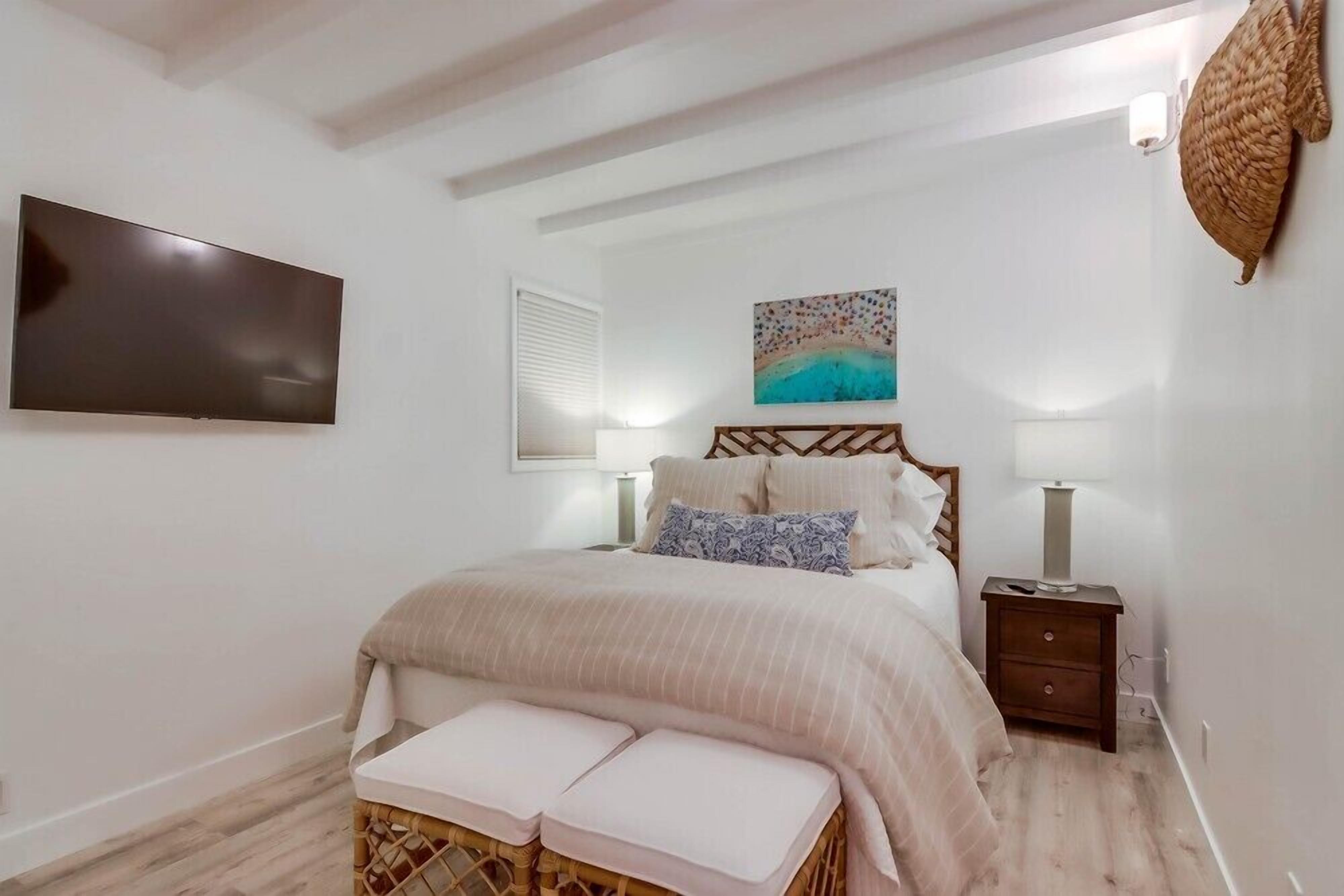 A bedroom with a bed, bedside tables, a TV, and a painting on the wall.