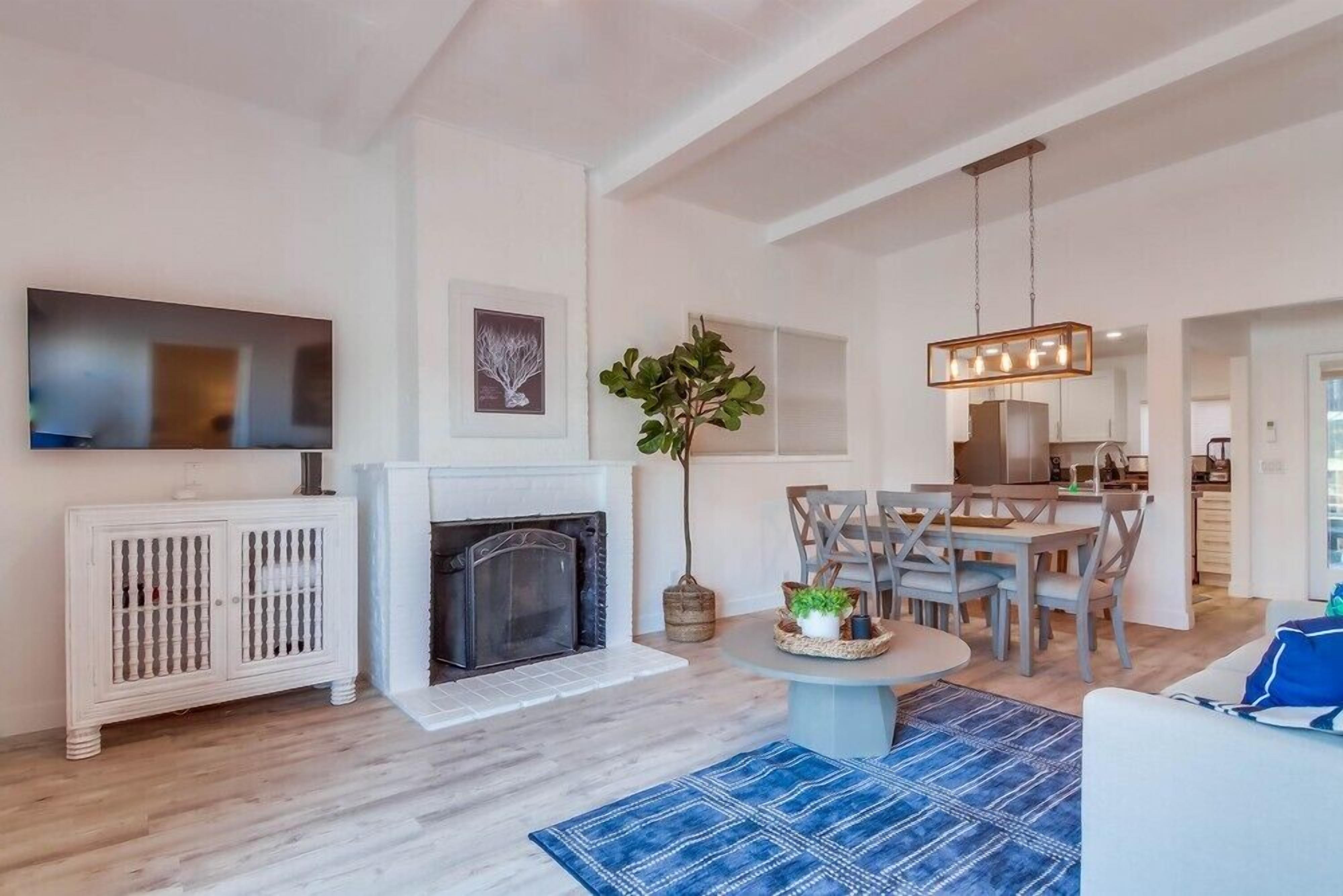 A modern living room with a fireplace, dining area, and kitchen in the background.