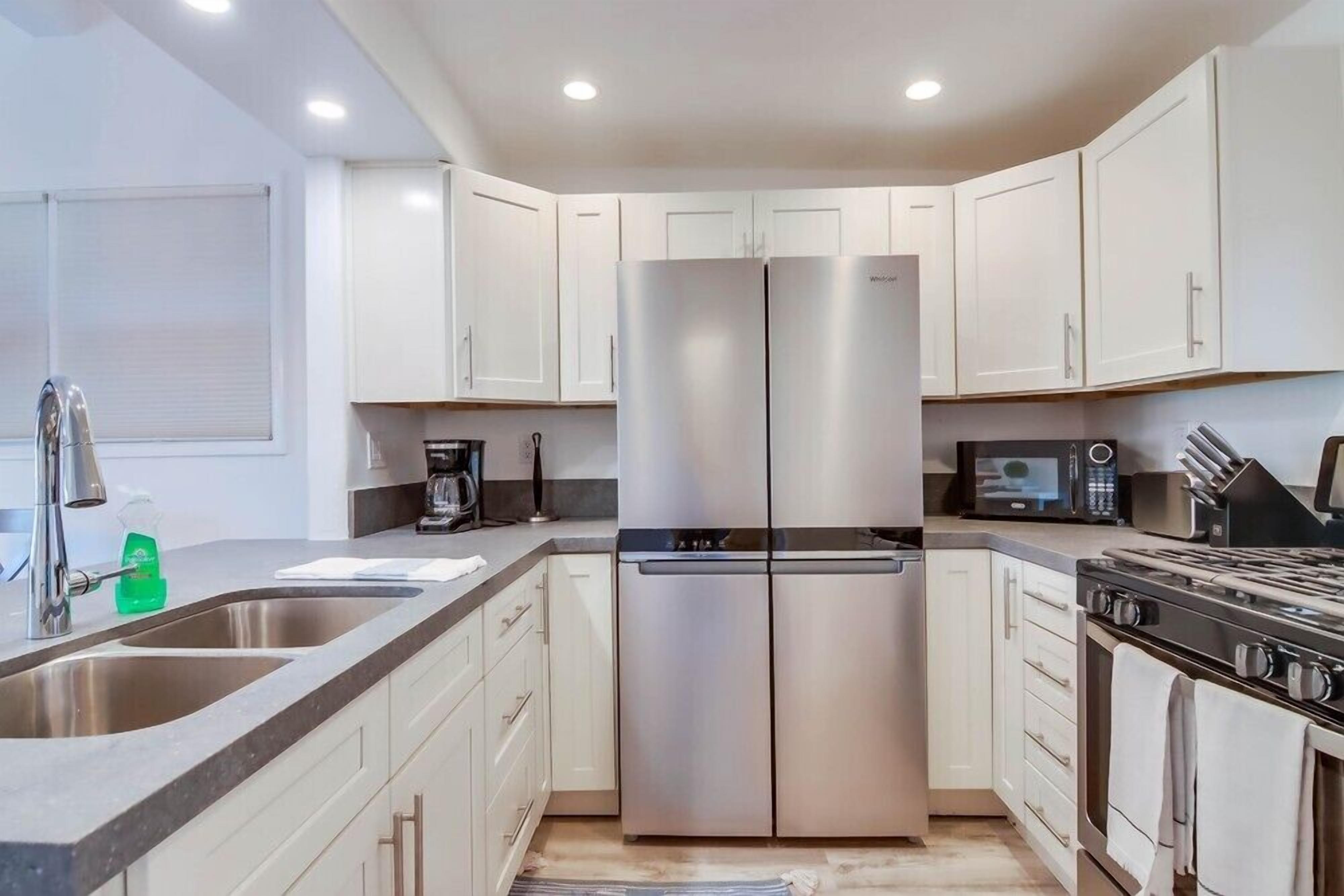 A modern kitchen with stainless steel appliances, white cabinetry, and a large island with a sink.
