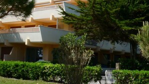 A multi-story hotel with a flat roof, balconies, and a well-maintained garden with various shrubs and a small tree.