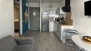A modern kitchen with a built-in oven, microwave, and coffee maker. There is a dining table with chairs and a grey sofa in the living area.