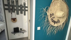 A room with a teal accent wall, a wooden stool, a laptop on a shelf, and a straw hat with text.