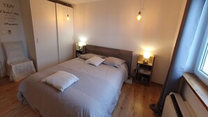 Un dormitorio ordenado con una cama grande, mesitas de noche con lámparas, un armario y una ventana con cortinas.