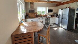 Una cocina con vigas de madera, una mesa redonda de madera y un refrigerador.