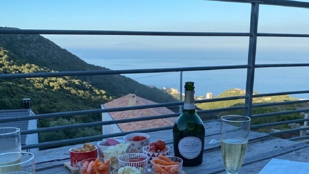 Una mesa de madera con una botella de vino blanco, copas y varios aperitivos.