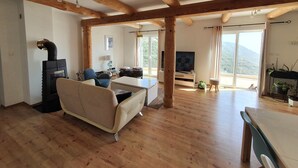 Amplia sala de estar con vigas de madera, un sof á, televisor y chimenea.
