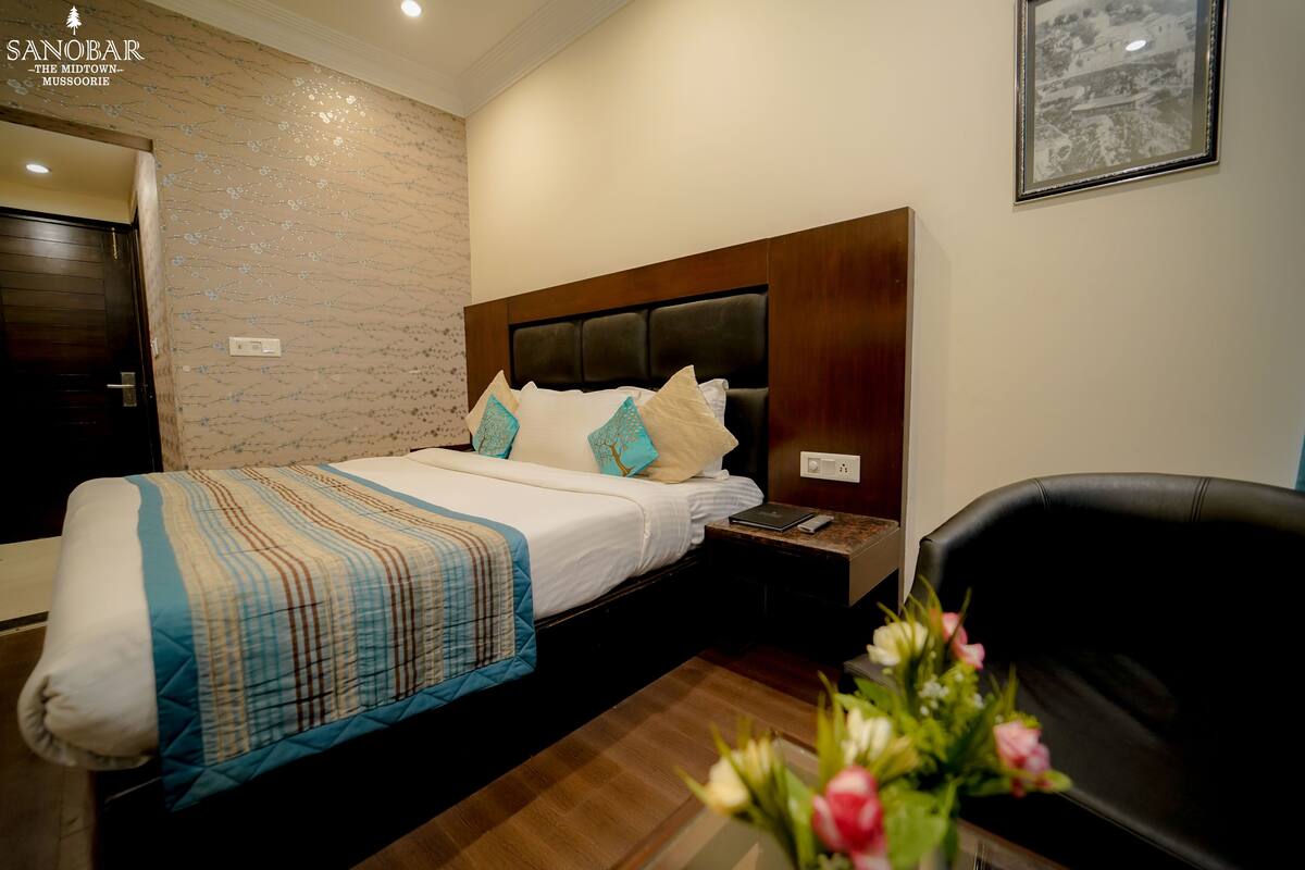 A hotel room with a bed, a nightstand, a chair, and a wall-mounted picture.