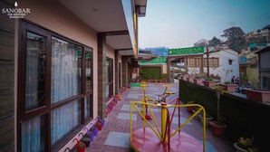 Un hotel con un área exterior cubierta que incluye un espacio de juegos para niños, plantas en macetas y un letrero del Grupo Hotelero Sanobar.