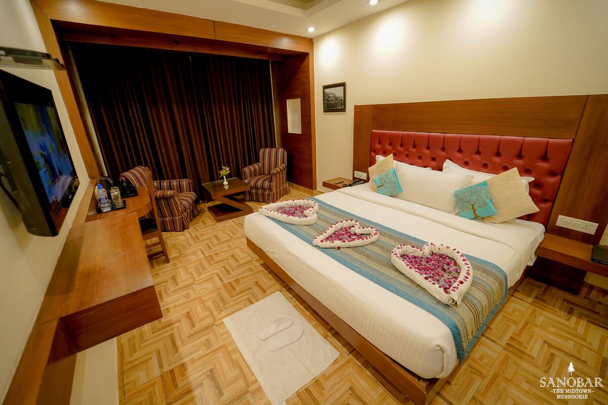A hotel room with a large bed, a TV, a seating area with chairs, and a wooden floor.