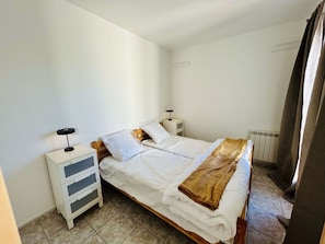 A single bed with a wooden frame, white bedding, a bedside table with a lamp, and a radiator.