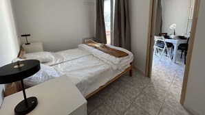 Une chambre à coucher avec un lit, une table de chevet, une lampe et une vue sur un coin repas, accessible par une porte ouverte.