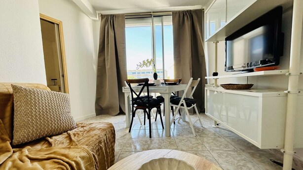 Un espace de vie compact comprenant un canapé, une table à manger avec des chaises, un téléviseur posé sur un meuble et une vue par la fenêtre.