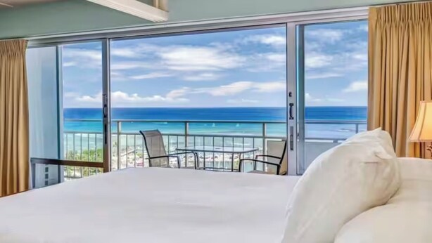 A hotel room with a large bed, a balcony with a view of the ocean, and a seating area with chairs. - Oceanfront Waikiki/Ilikai Condo w/Stunning View and Parking Included! (honolulu)