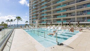 A rooftop pool with clear blue water, surrounded by lounge chairs and umbrellas, overlooking a cityscape and palm trees. - Oceanfront Waikiki/Ilikai Condo w/Stunning View and Parking Included! (honolulu)