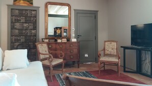 Una habitación con una cama, dos sillones, un aparador de madera, un espejo grande, un televisor y una estantería.