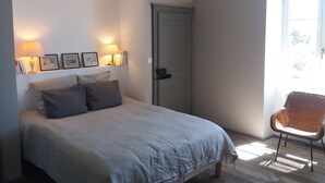 Un dormitorio con una cama, dos lámparas de noche, una silla y una puerta.