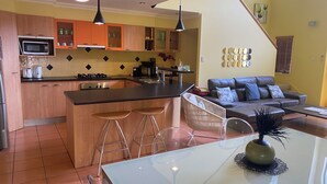 Une cuisine moderne avec des meubles en bois, un îlot central, des tabourets de bar et une table à manger agrémentée d’un vase.