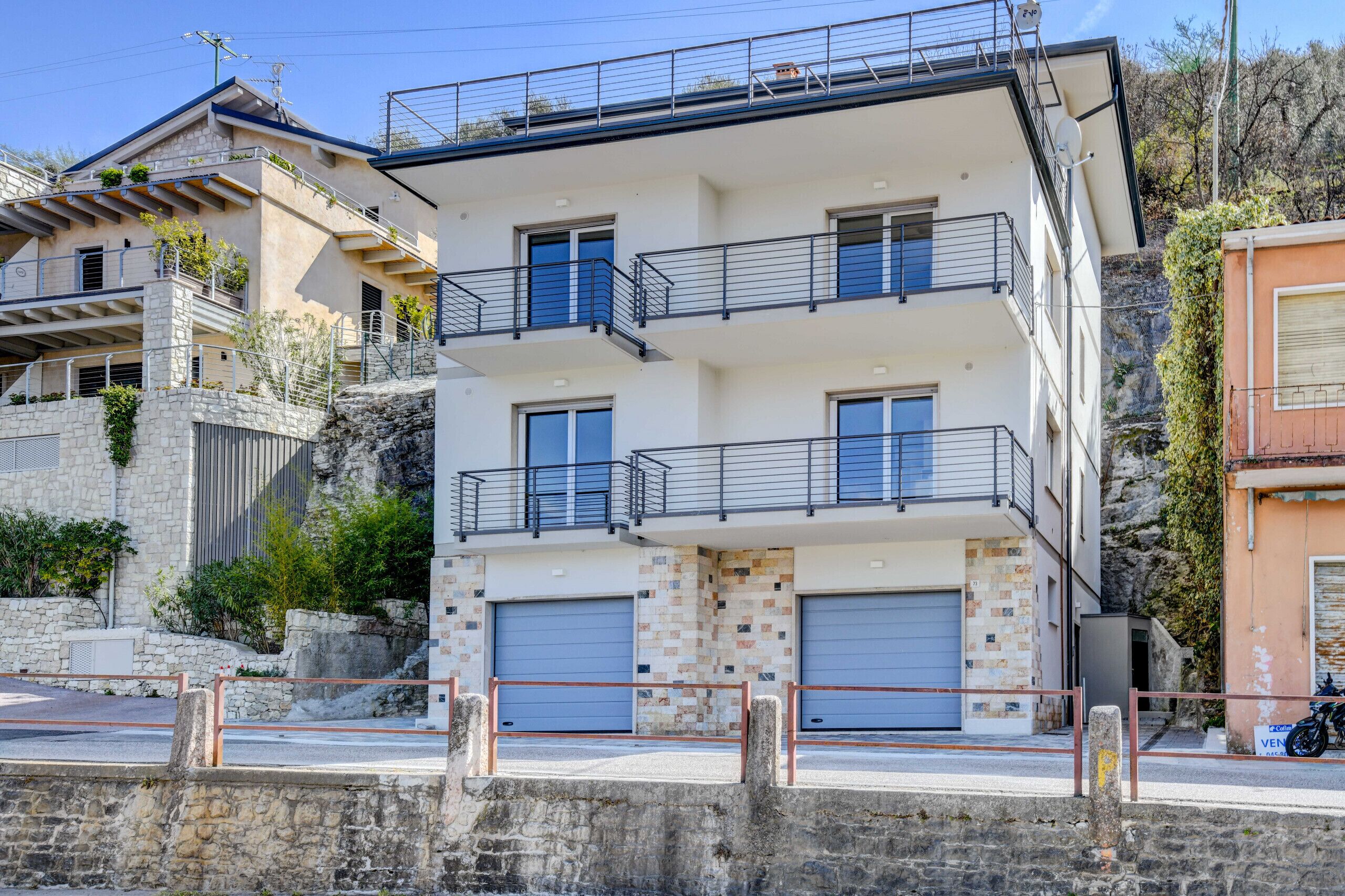 Un immeuble résidentiel à plusieurs étages, doté de balcons, de portes de garage et d’un mur en pierre.