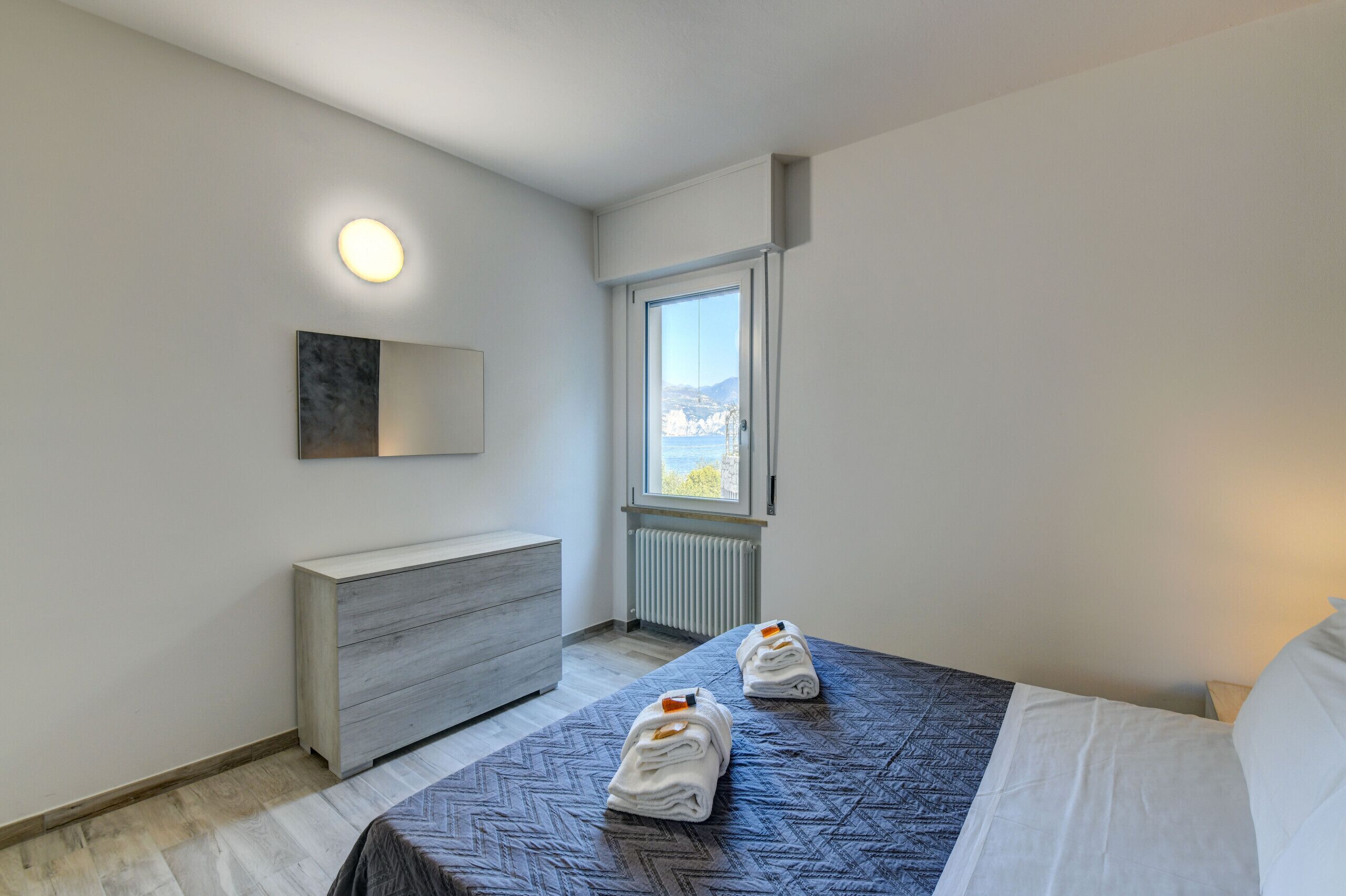 Une chambre d’hôtel moderne, équipée d’un lit, d’une commode, d’un radiateur et d’une fenêtre donnant sur un paysage agréable.