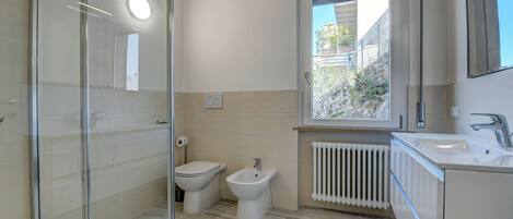 A modern bathroom with a glass shower enclosure, a bidet, a toilet, and a sink with a mirror above it.