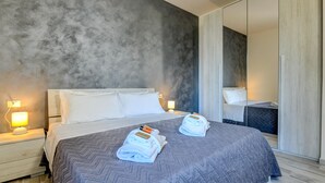 A modern hotel room with a large bed, two bedside tables with lamps, a wardrobe, and a mirror. - Holiday Apartments Brenzone - Apartment SOLE (Brenzone)