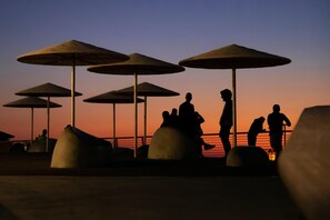 A sunset scene with beach umbrellas and people sitting on large concrete structures. - Silicate Ben Yehuda - Smart Hotel by Loginn Tel Aviv (Tel Aviv)