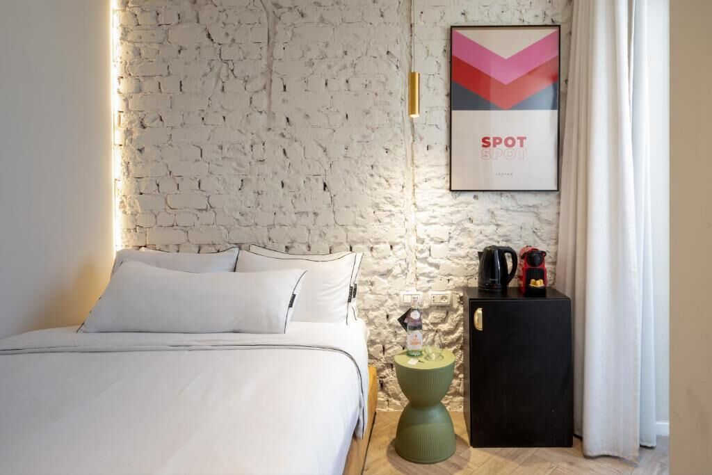 A bedroom with a white brick wall, a bed with white bedding, a green side table, a black cabinet, and a framed picture on the wall.