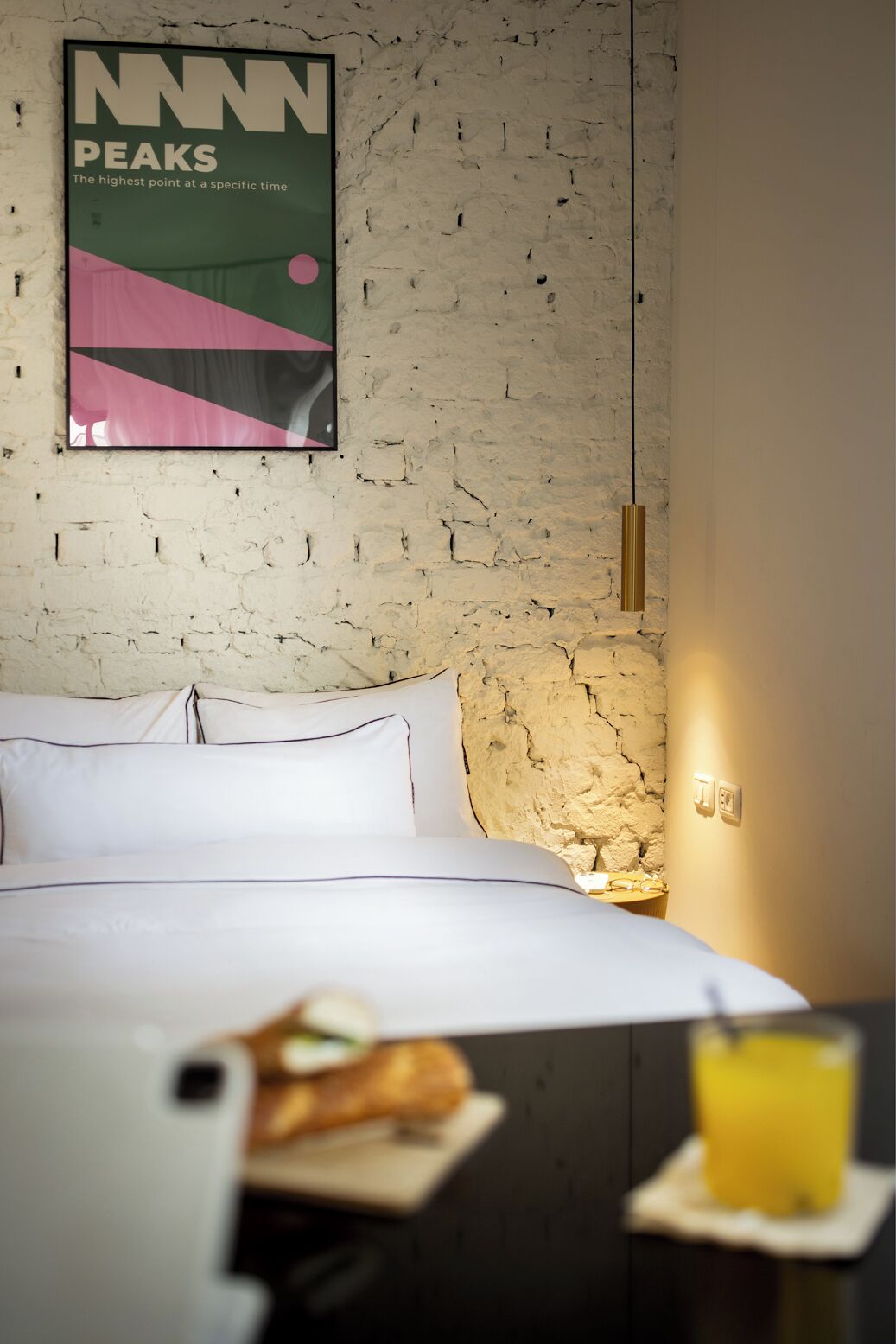 A hotel room with a bed, a poster on the wall, a nightstand, and a breakfast tray with toast and juice.