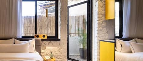 A bedroom with a large bed, a small round table, a yellow cabinet, and a sliding glass door leading to an outdoor area.