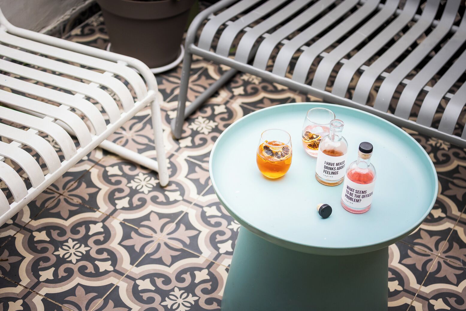 A table with a light blue top, two glasses of amber liquid with dried fruit, and two bottles with labels.