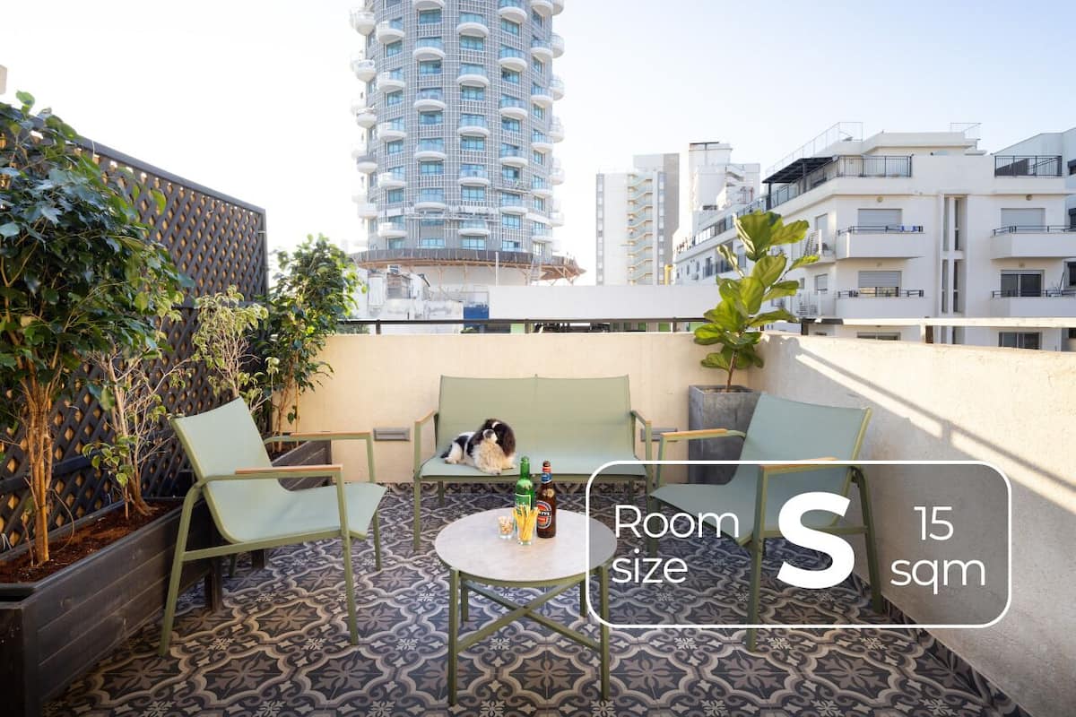 A rooftop terrace with a small table and two chairs, surrounded by plants and a patterned floor.