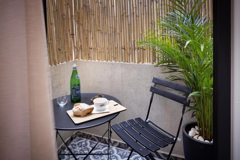 A small outdoor seating area with a table, a chair, a potted plant, and a bottle of beer.