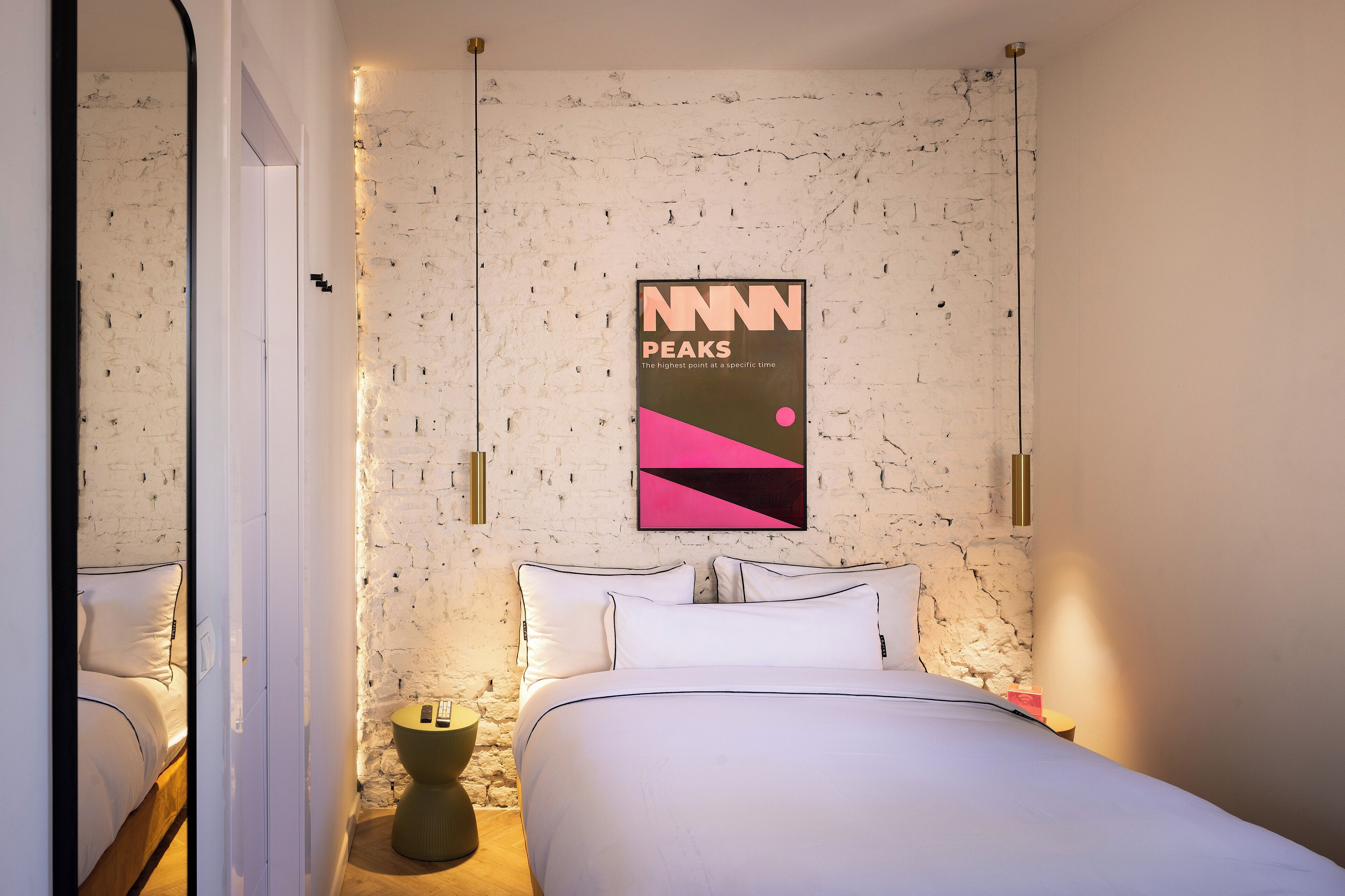 Ein modernes Schlafzimmer mit weißer Ziegelwand, einem Bett mit weißer Bettwäsche, einem Poster an der Wand und einem kleinen runden Tisch mit einer Lampe.